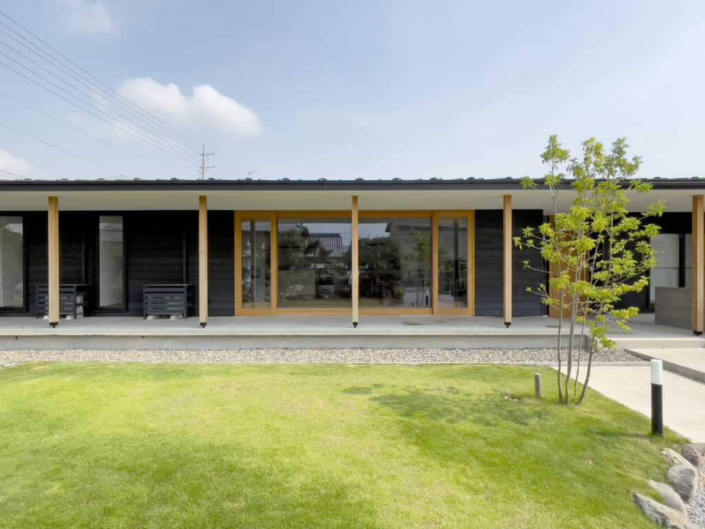 芝生の庭越しに見る『八幡の平屋』の正面外観。大開口の窓と深い庇が内外をつなぐ開放的なデザイン